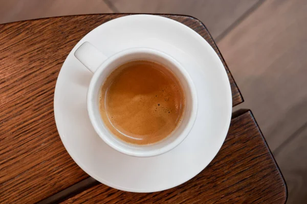 Italian espresso in a white ceramic cup with saucer on a brown w — Stock Photo, Image