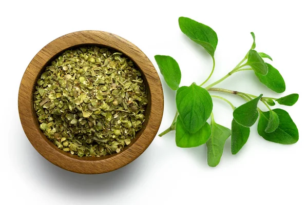 Dried chopped oregano in dark wood bowl next to fresh oregano le — Stock Photo, Image