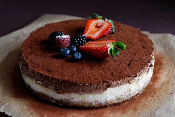 Whole homemade cheesecake on baking paper with cocoa and fruit t — Stock Photo, Image