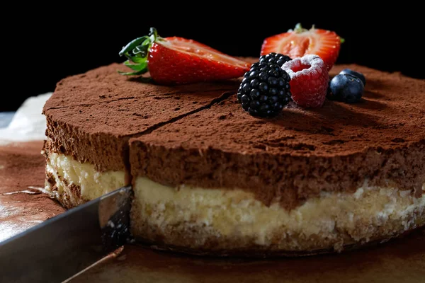 A knife cutting a slice of homemade cheesecake on baking paper w — Stock Photo, Image