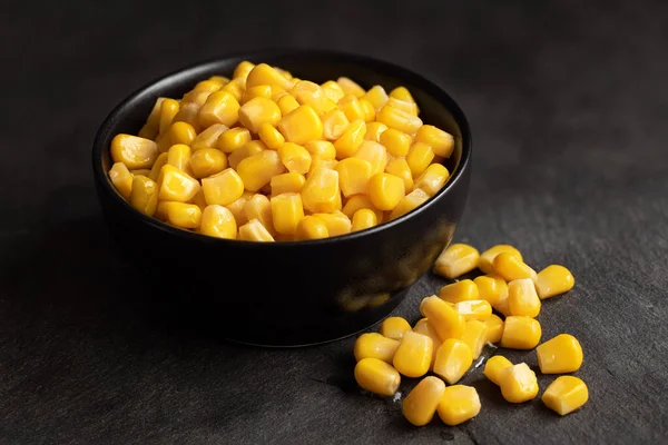 Canned sweet corn in a black ceramic bowl isolated on black slat
