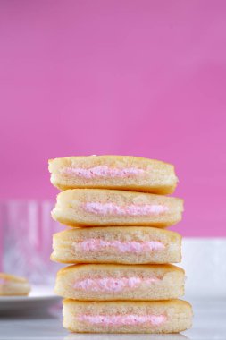 Mini kekler istiflenmiş ve ikiye bölünmüş. İçini ve çilek kremasını gösteriyor..