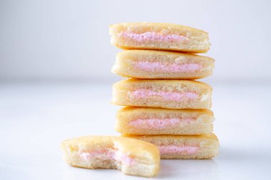 Mini kekler istiflenmiş ve ikiye bölünmüş. İçini ve çilek kremasını gösteriyor..