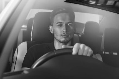 Bir arabada oturan ve direksiyon tutan yakışıklı adam.