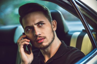 Yakışıklı adam arabanın arka koltuğunda oturmak ve bir telefon kullanma.