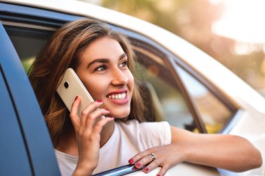 Telefonu arabada arka koltukta otururken gülümseyen güzel kadın.