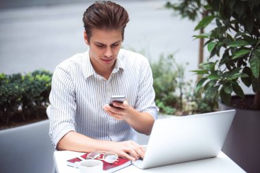 Akıllı tutum. Bir dizüstü bilgisayar kullanarak ve internet'te sörf yaparken kafede oturan olumlu yakışıklı adam.