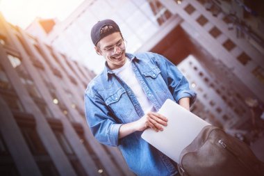 Bilgisayar ekranına bakarak seyir vasıl belgili tanımlık defter Sokağı'nda oturan genç bir şey açık havada, iş molası sırasında dizüstü klavyede yazarken mutlu yakışıklı öğrenci.