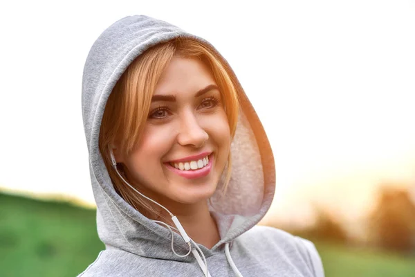 Beautiful young woman with headphones glad after nice jogging in city park