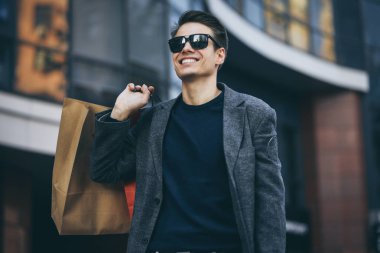 Ciddi cool adam güneş gözlüğü ve kağıt torbalar street yürüyüş.