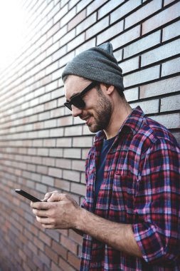 Hipster sms manifatura telefon app şehirdeki sokak üzerinde tuğla duvar arka plan. Smartphone akıllı rahat kıyafet ayakta tutan inanılmaz bir adam. Kentsel genç profesyonel yaşam tarzı.