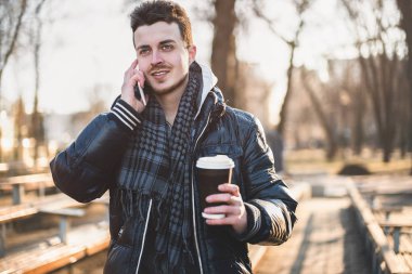 Beyaz adam sokakta cep telefonu bakıyor.