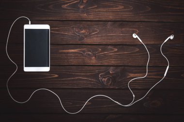 Kulaklığı ahşap arka planda olan beyaz akıllı telefon. Görüntü. Müzik çalınıyor