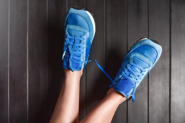 Close up immagine di moda dei piedi della donna, indossando scarpe da ginnastica sportive su sfondo di legno. concetto di donna pigra. concetto di riposo. lacci delle scarpe slacciati — Foto Stock