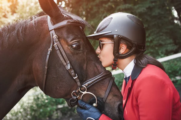 A young girl jockey talking and kissing her horse. She loves the animals and joyfully spends her time in their environment.