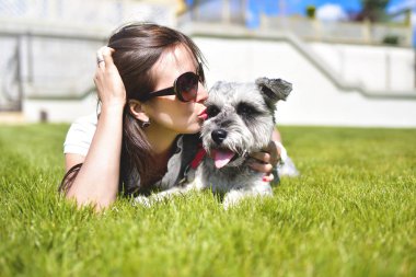 Güzel yetişkin beyaz mutlu kadın sevgili köpeği ile güneşli bir günde parkta istirahat. Dişi çimenlerin üzerinde yatıyor, gülümsüyor ve kameraya bakıyor. aşk hayvanları kavramı