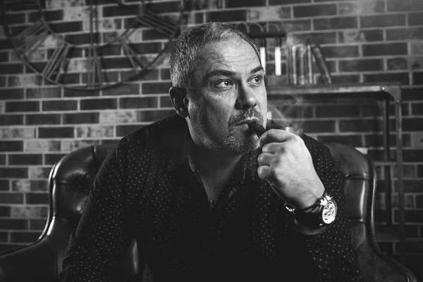 Hombre de negocios adulto serio se sienta en su oficina y fuma una pipa — Foto de Stock