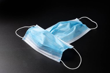 Plastik kulaklıklı mavi tıbbi maske. Siyah arka planda tipik 3 katlı cerrahi maske, Corona virüs koruma konsepti. Sağlık sigortası COVID-19 pandemik karantina.