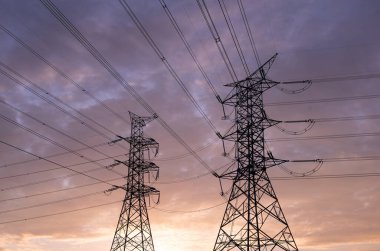 Yüksek voltajlı elektrik direklerinin ve çizgilerin silueti, günbatımı gökyüzü arka planında yüksek voltajlı elektrik iletim kulesi..