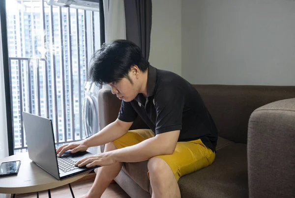 Asian businessman sitting on a sofa at home and working on a laptop. work from Home concept.