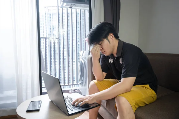 Stressed asian businessman sitting on a sofa at home and working on a laptop. tired man work from Home concept.