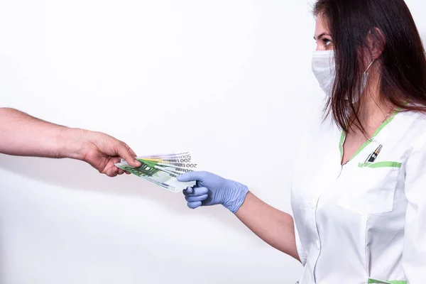 Hand of patient giving paper currency to female doctor against white background — Stock Photo, Image
