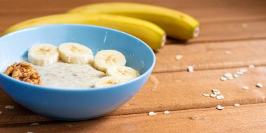 Yukarıdan manzara. Tahta bir masada, muzlu yulaf ezmesi ve kahvaltıda ceviz, yakın plan.