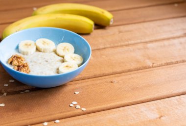 Yukarıdan manzara. Tahta bir masada, muzlu yulaf ezmesi ve kahvaltıda ceviz, yakın plan.