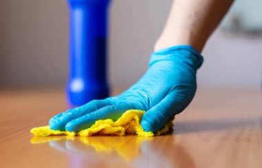 Gri kazaklı ve mavi eldivenli bir kız sarı bir bezle ahşap bir masayı yıkıyor..