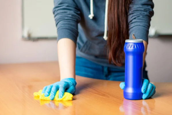 Girl in a gray sweater and blue gloves washes a wooden table with a yellow rag. — Stock Photo, Image