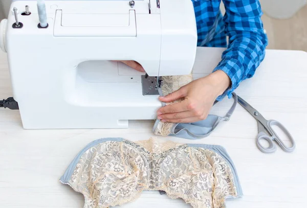 Una costurera alegre con una camisa de cuadros azules está trabajando en su taller. primer plano, ella está cosiendo ropa interior de encaje de las mujeres . —  Fotos de Stock