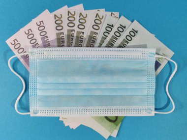 Bir tıbbi maske ve hediye kutusu 100, 200 ve 500 Euro 'luk banknotlar ve bir fotokopi alanı, mavi arka plan üzerine yerleştirilir..