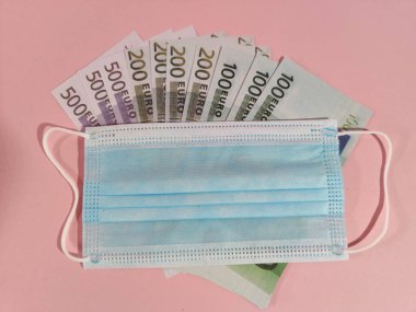 Bir tıbbi maske ve hediye kutusu 100, 200 ve 500 Euro 'luk banknotlar ve bir fotokopi alanı, mavi arka plan üzerine yerleştirilir..