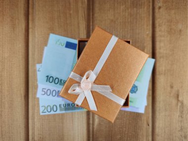 Küçük bir hediye kutusu biraz aralıktır ve 200 ve 500 Euro 'luk banknotların üzerinde ve ahşap bir arka planda bir fotokopi alanı bulunur. tahta tahtaların arkaplanı