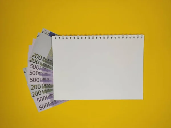 На желтом фоне, блокнот с копировальным местом, купюры 200 и 500 евро выглядывают из-под него . — стоковое фото