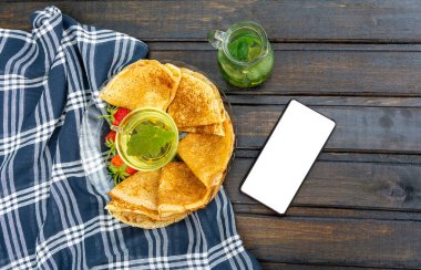 Bir tabak krep ve çilek kareli havluyla kaplı ahşap bir masada oturur. Bir fincan da kuşüzümü ve nane yapraklı çay. Telefonda kopyalama alanı var..