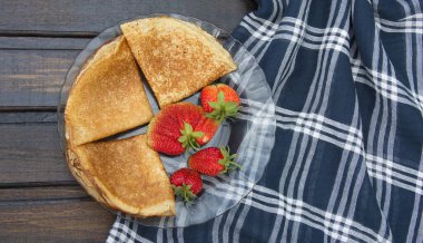 Kareli masa örtüsüyle kaplı ahşap bir masanın üzerinde krepli bir tabak var ve çileğin ortasında...