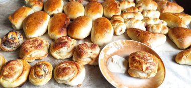 Beyaz mutfak masasında haşhaşlı çörekler, köfteler ve bir tabak ekşi krema var..