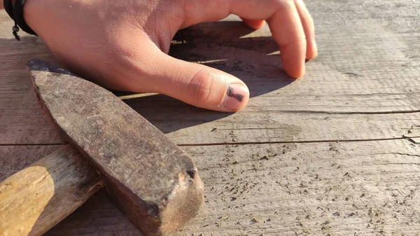 Bir çekiç ve eski ahşap bir masanın arka planında siyah bir çivi izi olan bir parmak. Çok acı verici. Yüksek kalite fotoğraf