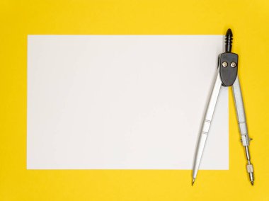 Sarı arka planda, beyaz bir kağıt ve bir pusula, okul derslerinin başlangıcı konsepti. Uzayı kopyala Yüksek kalite fotoğraf