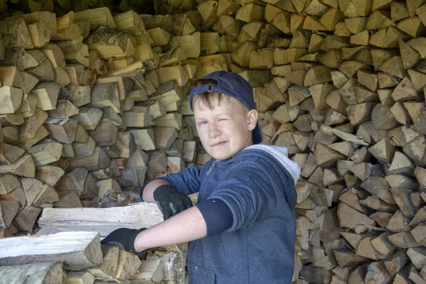 Barn stapla upp hackad torr ved. Pojke på bakgrunden av hackad ved. Vintertimmer från björk och tall. — Stockfoto