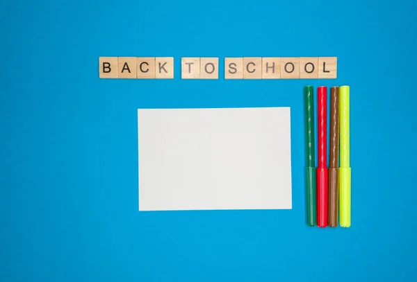 Sobre un fondo azul, una hoja de cuaderno, marcadores de colores y una frase hecha de letras de madera, de vuelta a la escuela, el concepto de volver a la escuela después de las vacaciones . — Foto de Stock