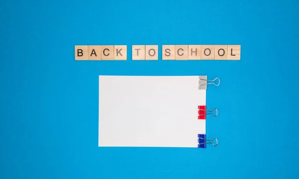 Sobre un fondo azul, una hoja de cuaderno y una frase hecha de letras de madera, de vuelta a la escuela, el concepto de volver a la escuela después de las vacaciones . — Foto de Stock