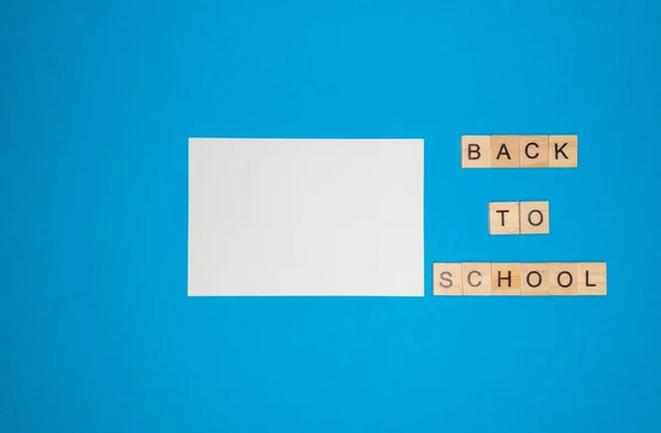 На синем фоне, блокнот и фраза из деревянных букв, вернуться в школу, концепция возвращения в школу после каникул. — стоковое фото
