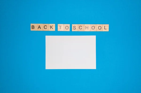 Sobre un fondo azul, una hoja de cuaderno y una frase hecha de letras de madera, de vuelta a la escuela, el concepto de volver a la escuela después de las vacaciones . — Foto de Stock
