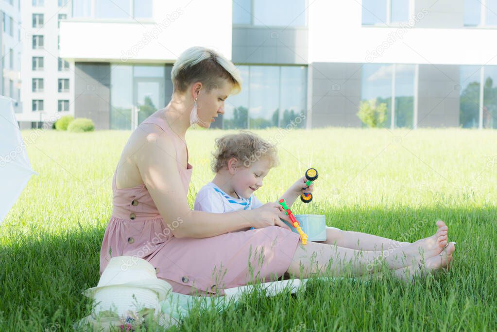 A young woman sitting in the grass. A child is sitting next to her. They play with toys. 