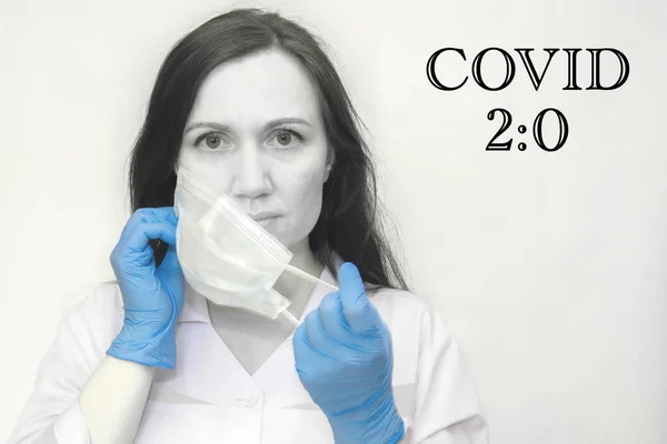 Siyah ve beyaz fotoğraf, tıp eldivenli genç bayan doktor yüzüne koruyucu bir maske takıyor. Covid 2: 0 afişindeki yazı. Covid-19 Coronavirüs 'ün ikinci dalgası..