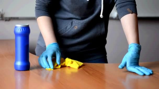 Meisje in een grijze trui en blauwe handschoenen wast een houten tafel met een gele doek. — Stockvideo