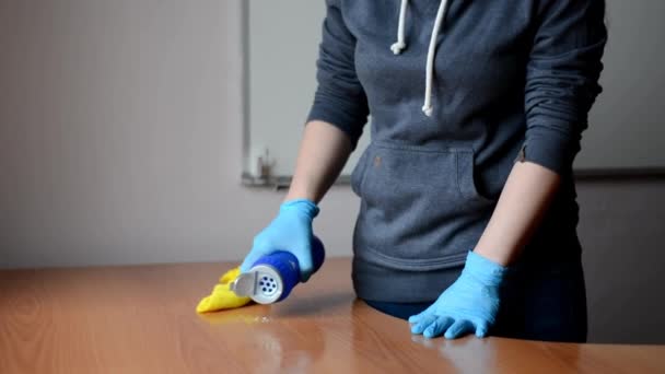 Una niña en un suéter gris y guantes azules está lavando una mesa de madera con un trapo amarillo. Ella derrama detergente sobre la mesa y la limpia con un trapo. — Vídeos de Stock