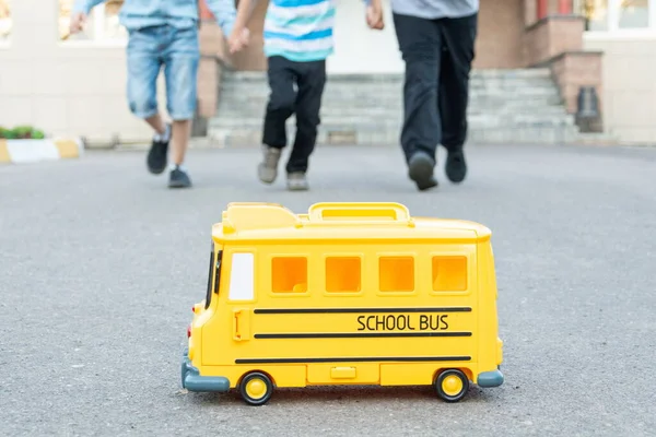 In the foreground is a yellow toy school bus, with children running towards it in the background. back to school concept. — Stock Photo, Image
